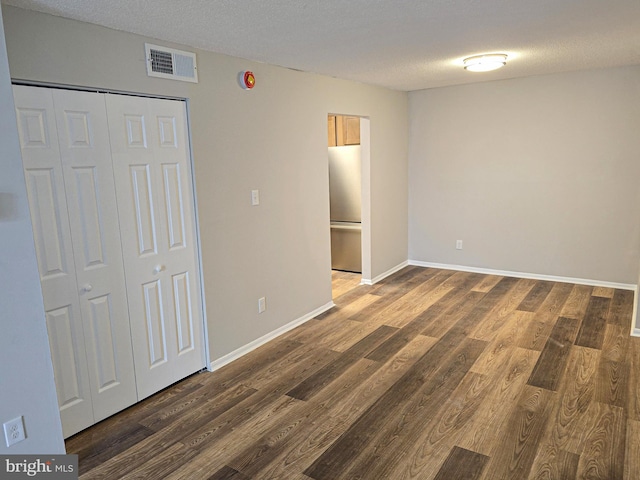 unfurnished bedroom featuring visible vents, a textured ceiling, wood finished floors, and freestanding refrigerator