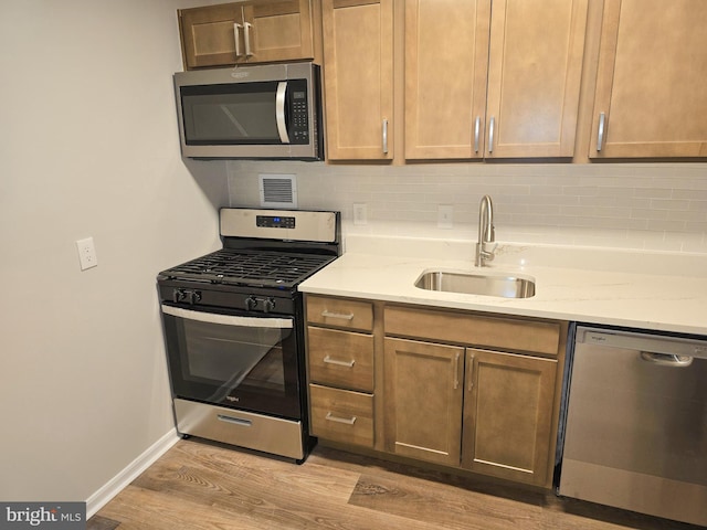 kitchen with a sink, light stone counters, tasteful backsplash, stainless steel appliances, and light wood finished floors