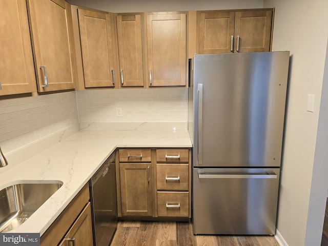 kitchen with a sink, backsplash, wood finished floors, stainless steel appliances, and light stone countertops