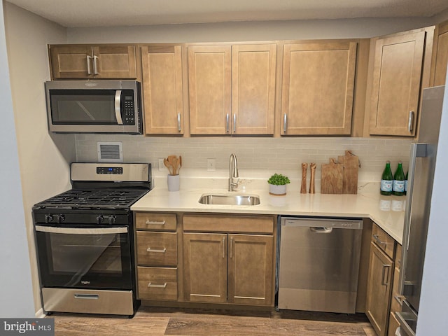 kitchen with backsplash, appliances with stainless steel finishes, light countertops, and a sink