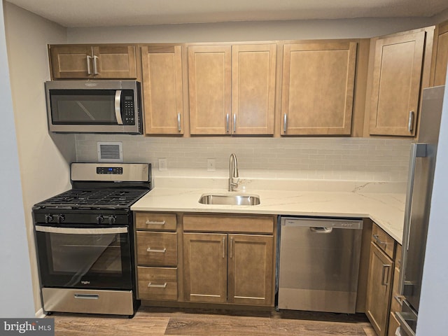 kitchen featuring a sink, stainless steel appliances, light stone countertops, and backsplash