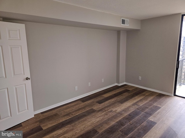 basement featuring visible vents, dark wood-type flooring, and baseboards