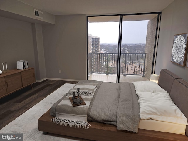 bedroom featuring wood finished floors, visible vents, baseboards, access to exterior, and expansive windows