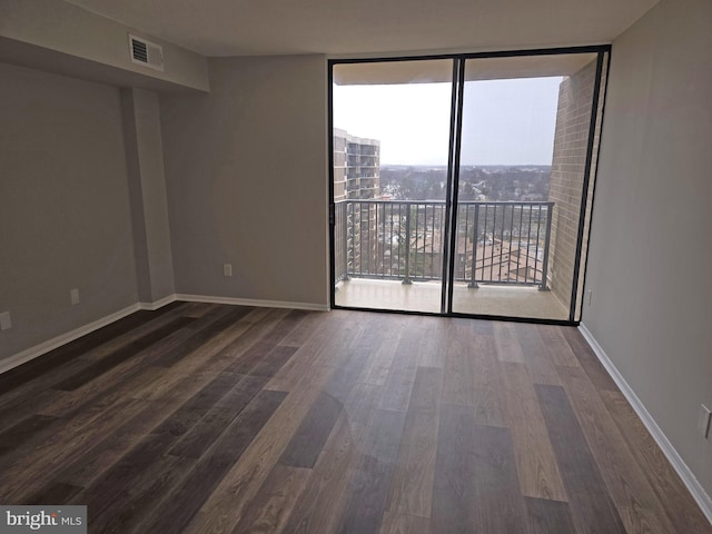 spare room with baseboards, wood finished floors, visible vents, and expansive windows