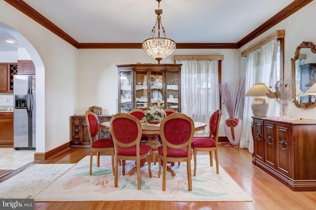 dining space with arched walkways, light wood-style flooring, baseboards, and ornamental molding