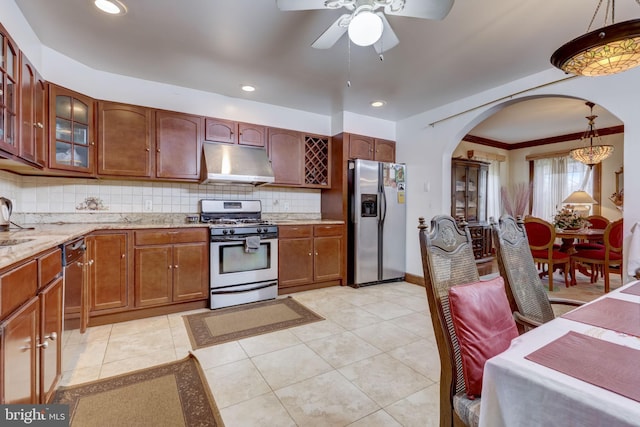 kitchen with under cabinet range hood, light stone counters, decorative backsplash, appliances with stainless steel finishes, and arched walkways