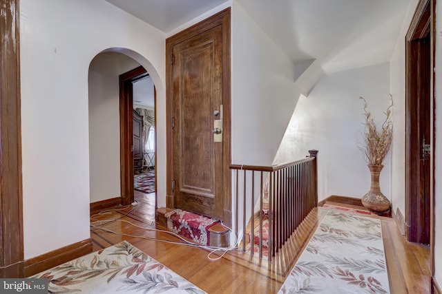 corridor with arched walkways, baseboards, and wood finished floors