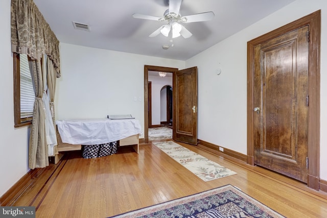 bedroom featuring visible vents, wood finished floors, arched walkways, baseboards, and ceiling fan