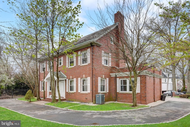 view of side of home featuring fence, central AC unit, brick siding, and a chimney