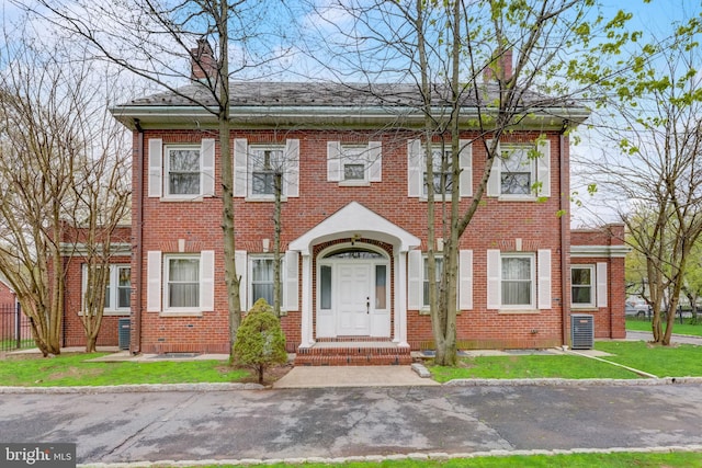 view of front of property featuring brick siding, a chimney, and a front yard