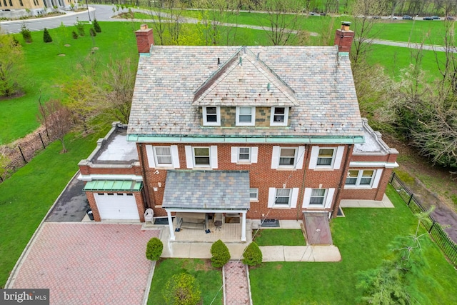 view of front facade featuring decorative driveway, a high end roof, a front yard, brick siding, and a chimney