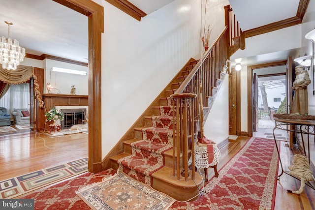 stairs with a glass covered fireplace, wood finished floors, a chandelier, and ornamental molding