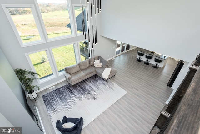 living area with visible vents, baseboards, a towering ceiling, and wood finished floors