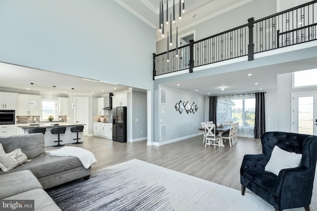 living area featuring visible vents, baseboards, light wood-style floors, and crown molding