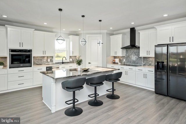 kitchen with a kitchen island, wall chimney range hood, a kitchen bar, appliances with stainless steel finishes, and white cabinets