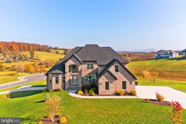 french country inspired facade with brick siding, a mountain view, a shingled roof, and a front lawn