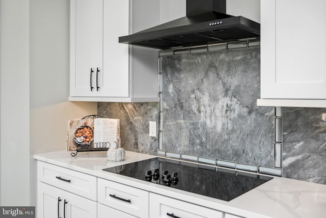 kitchen with backsplash, white cabinetry, wall chimney range hood, black electric cooktop, and light stone countertops