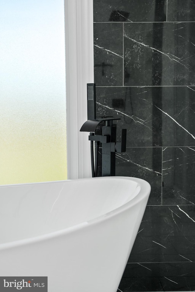 full bathroom with tile walls, a freestanding tub, and marble finish floor