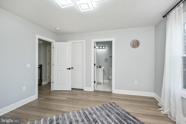 unfurnished bedroom featuring connected bathroom, baseboards, and wood finished floors