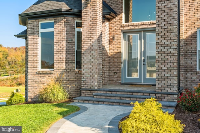 doorway to property featuring brick siding and roof with shingles