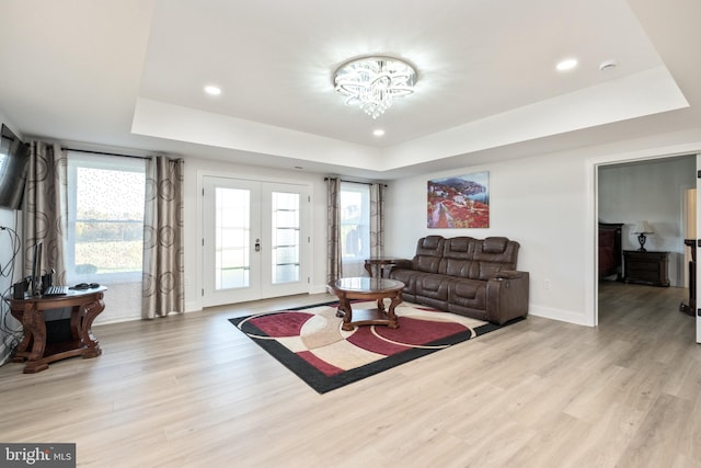 living room with a raised ceiling, plenty of natural light, french doors, and light wood-type flooring