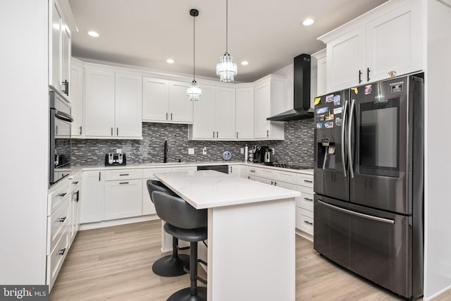 kitchen with light wood-type flooring, white cabinetry, stainless steel fridge, wall chimney exhaust hood, and light countertops