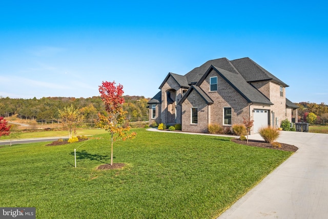 french country home featuring brick siding, a garage, concrete driveway, and a front yard