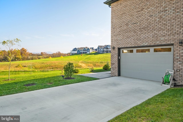 view of side of home with brick siding, a garage, concrete driveway, and a yard