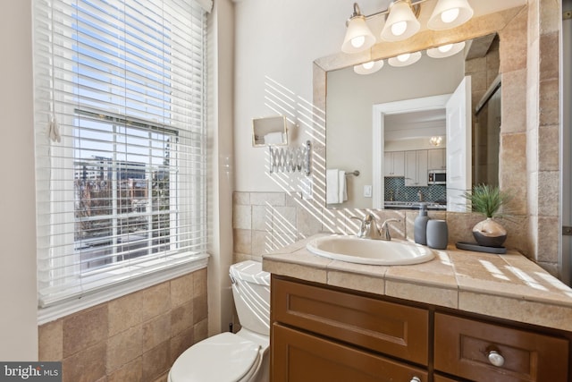 bathroom with vanity, tile walls, plenty of natural light, and toilet