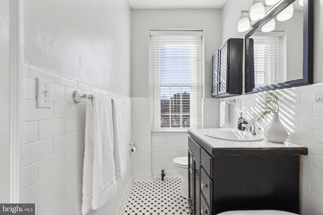 bathroom featuring wainscoting, toilet, tile walls, and vanity