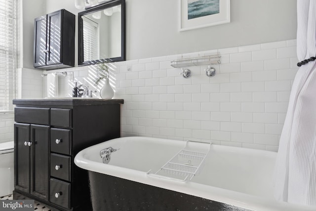 full bath featuring toilet, vanity, a freestanding bath, and tile walls