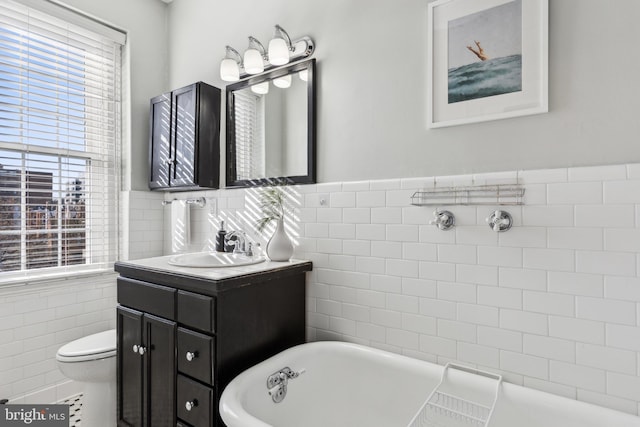 bathroom with vanity, a soaking tub, wainscoting, tile walls, and toilet