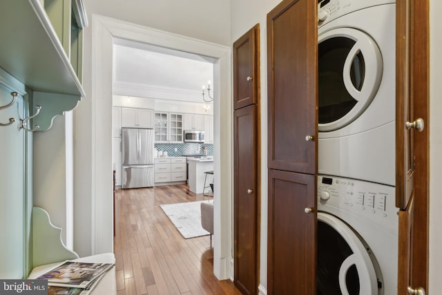 laundry room with stacked washer / dryer, cabinet space, and light wood-style flooring