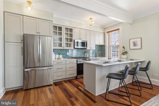 kitchen featuring backsplash, glass insert cabinets, appliances with stainless steel finishes, a peninsula, and dark wood-style floors