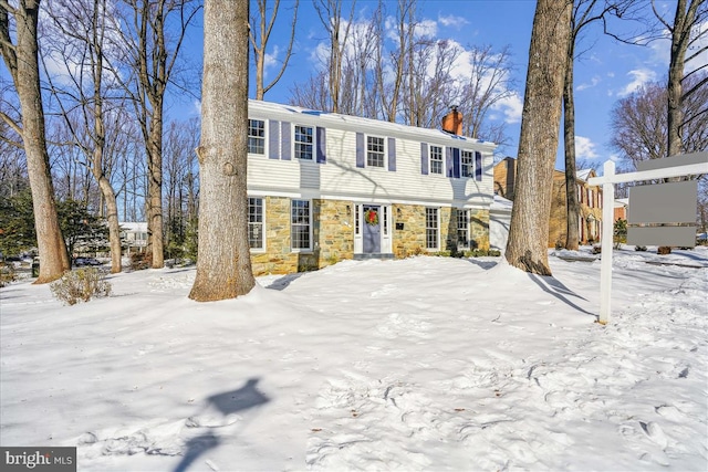 colonial-style house featuring stone siding and a chimney