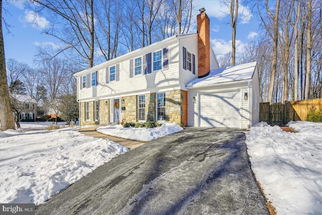 colonial inspired home with driveway, stone siding, fence, a garage, and a chimney