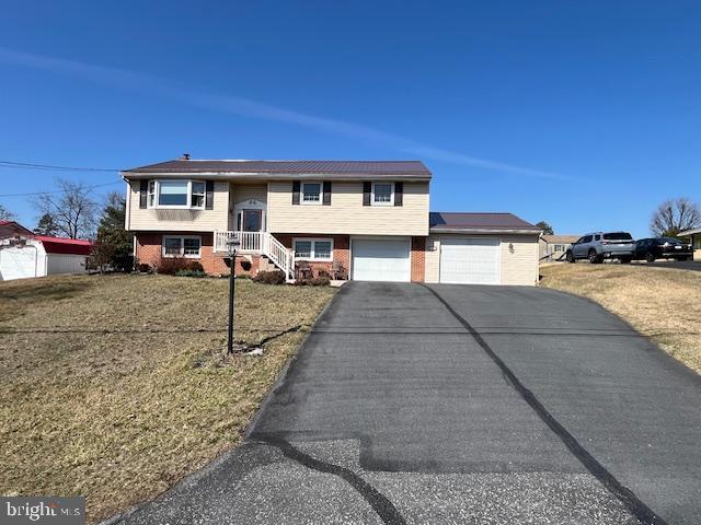 split foyer home featuring aphalt driveway, an attached garage, brick siding, and a front yard