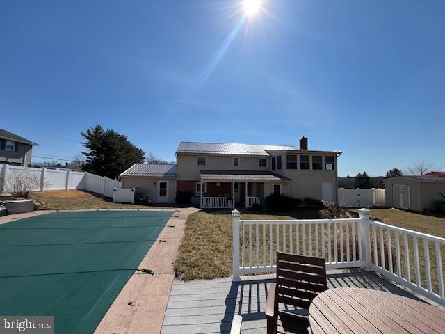 back of property with a fenced in pool, a deck, a fenced backyard, and a shed