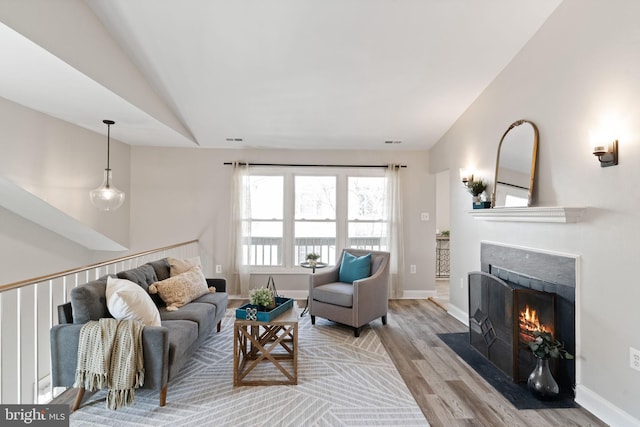 living area with lofted ceiling, a fireplace, baseboards, and light wood finished floors