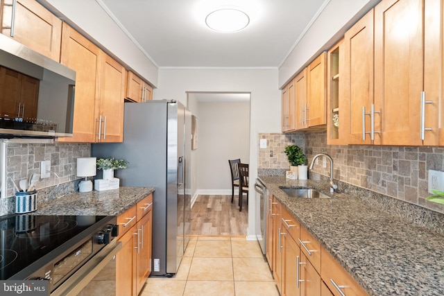 kitchen featuring light tile patterned floors, dark stone counters, a sink, appliances with stainless steel finishes, and crown molding