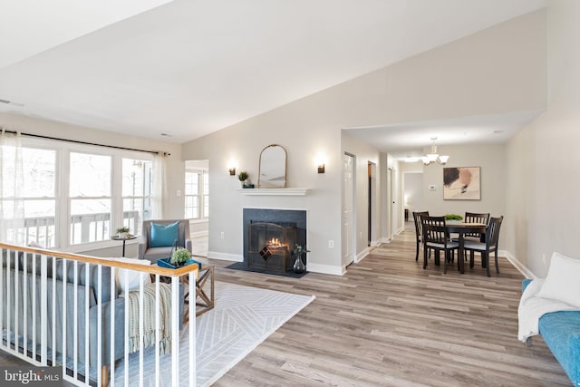 living area featuring baseboards, a fireplace with flush hearth, vaulted ceiling, wood finished floors, and a notable chandelier