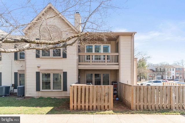 back of house featuring a balcony, central AC unit, a fenced front yard, and a chimney