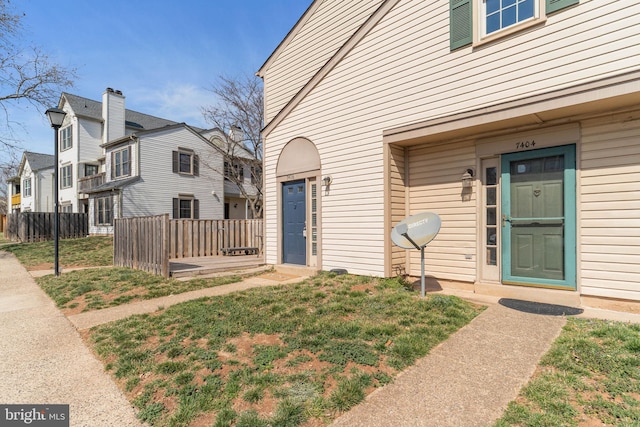 view of exterior entry with a yard, fence, and a residential view