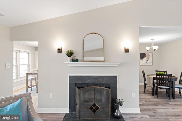 living area featuring a chandelier, a fireplace with flush hearth, baseboards, and wood finished floors