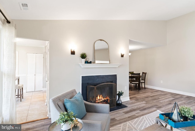 living room with visible vents, baseboards, a fireplace with flush hearth, vaulted ceiling, and wood finished floors