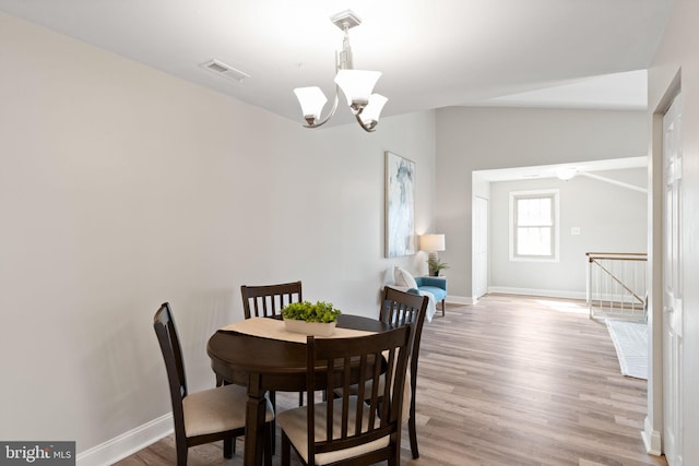 dining space featuring light wood-type flooring, visible vents, lofted ceiling, and a notable chandelier