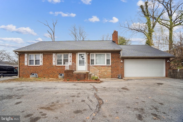 ranch-style house featuring driveway, a shingled roof, a garage, brick siding, and a chimney