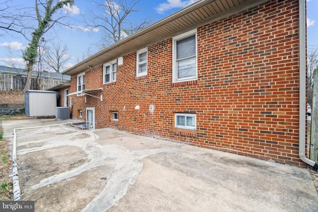 view of property exterior with a patio area, central AC unit, and brick siding