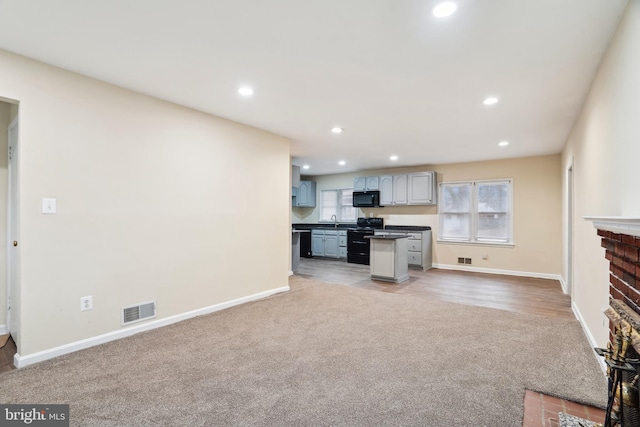 kitchen with dark countertops, visible vents, light colored carpet, black appliances, and a sink