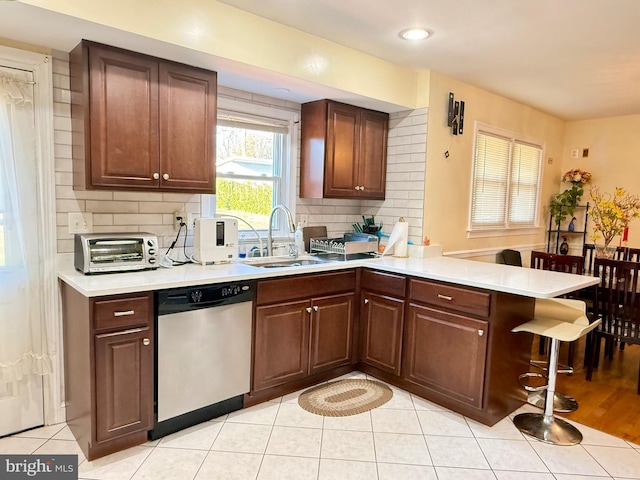 kitchen featuring a breakfast bar, a peninsula, a sink, light countertops, and dishwasher